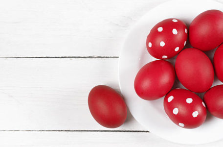 Traditional red and dotted Easter eggs in white plate on white wood background. Top view point.