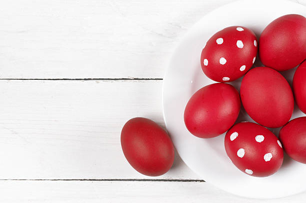 Traditional red and dotted Easter eggs in white plate on white wood background. Top view point.